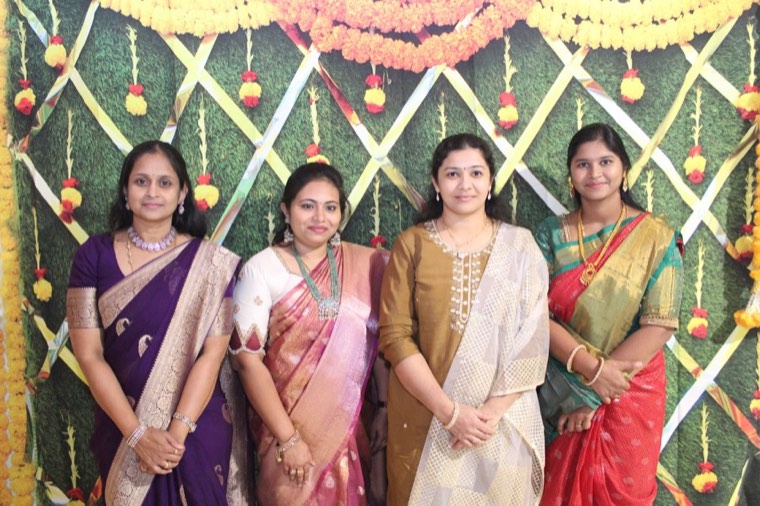 Members in festive sarees in front of the marigold backdrop at Deepavali 2024